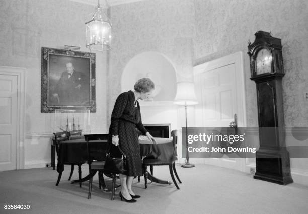 British Conservative prime minister Margaret Thatcher wipes crumbs off the table at 10, Downing Street, London, circa 1990. A painting of her...