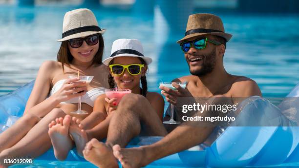 glückliche familie trinken coktail im schwimmbad - eltern sonnenbrille sonne lachen stock-fotos und bilder