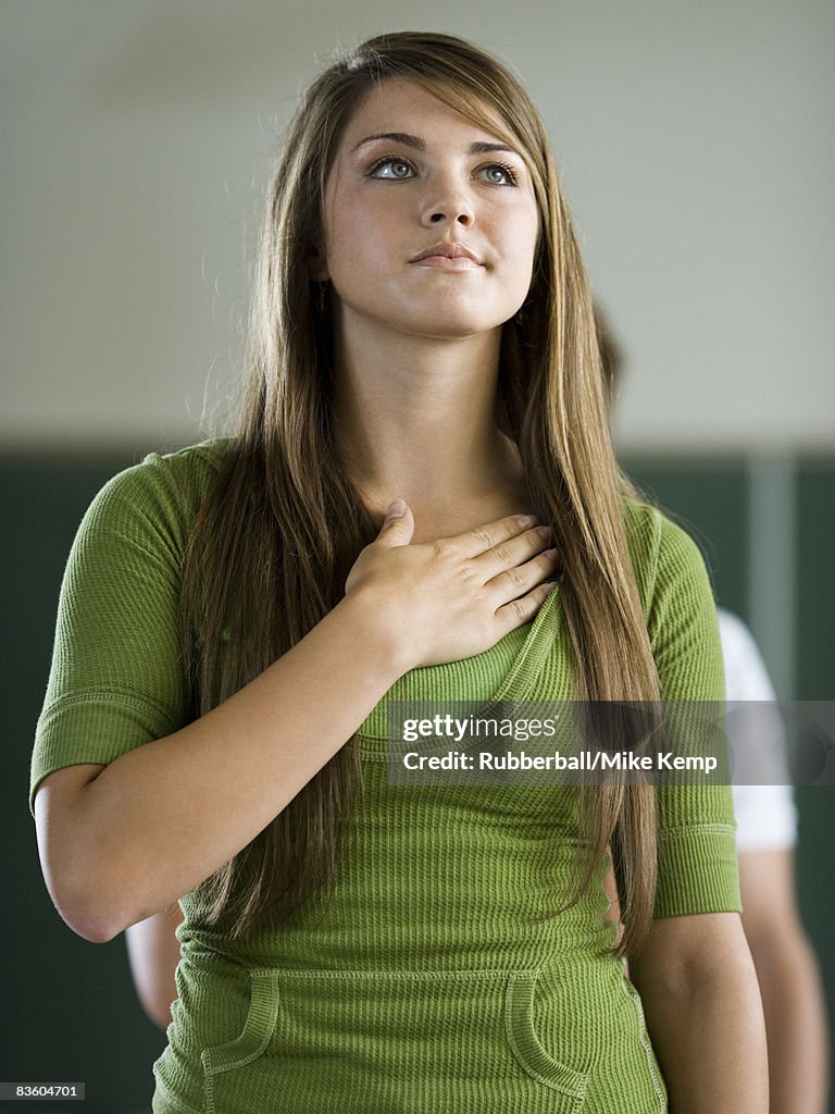Young woman in a classroom with hand over heart.