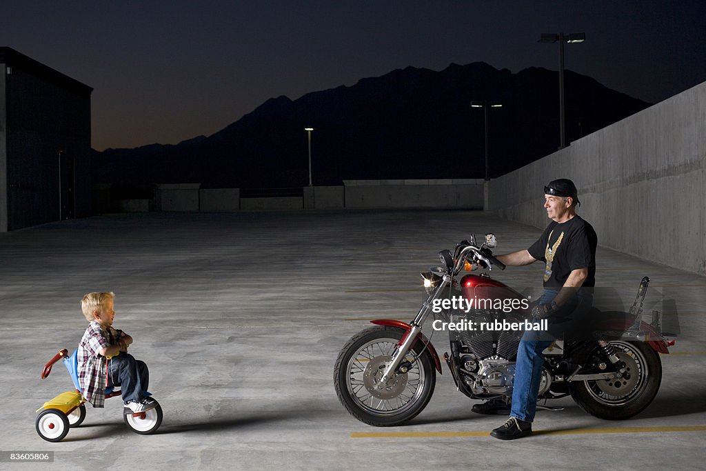 Boy on a tricycle next to a man on a motorcycle