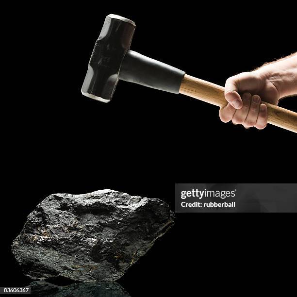 hand swinging a sledge hammer toward a piece of coal. - swinging sledgehammer stock pictures, royalty-free photos & images