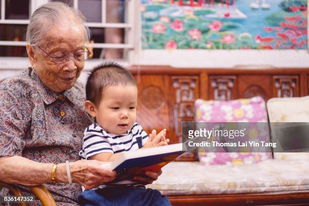 great grand mother reading story book to her great grandson joyfully - my lai sit stockfoto's en -beelden