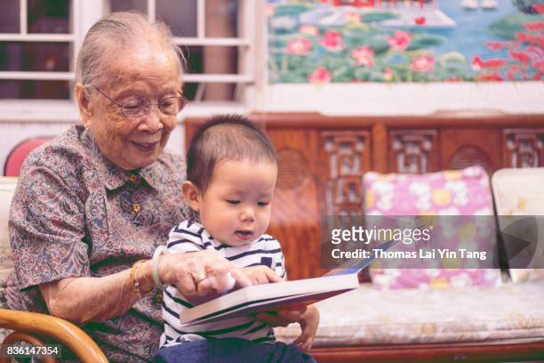 great grand mother reading story book to her great grandson joyfully - my lai sit stockfoto's en -beelden