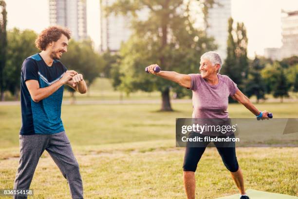 senior woman exercising with a personal trainer outdoors - hand weight stock pictures, royalty-free photos & images