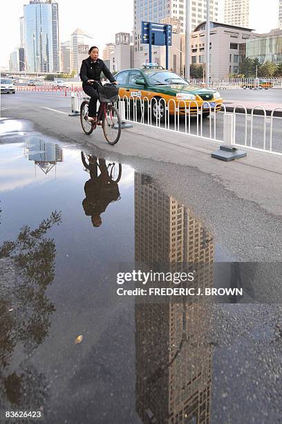 Cyclist refelcted in a roadside puddle, is dwarfed by the Yintai Center, a 249.9-metre high building in Beijing's CBD , built as a comibination of a...