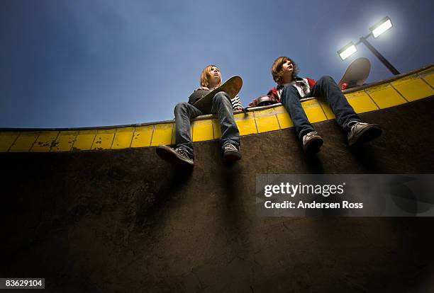 two boys sitting on the edge of skate park - boy skatepark stock-fotos und bilder