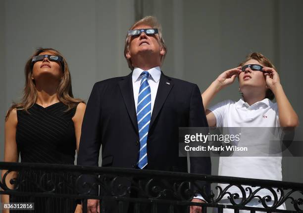 President Donald Trump, first lady Melania Trump and their son Barron Trump wear special glasses to view the solar eclipse from the Truman Balcony at...