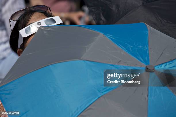 Woman wears solar viewing glasses and holds an umbrellas while looking at the sun during a solar eclipse viewing event on the campus of Southern...