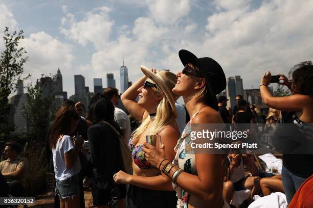 People watch a partial solar eclipse from the roof deck at the 1 Hotel Brooklyn Bridge on August 21, 2017 in the Brooklyn borough of New York City....