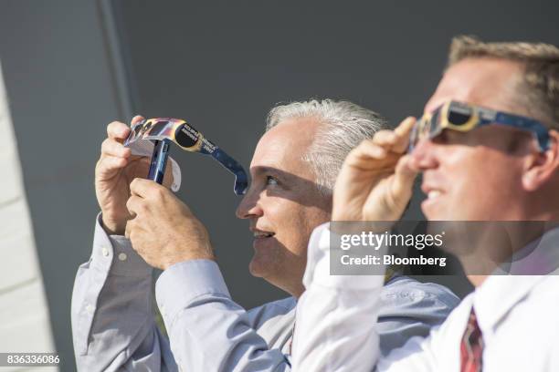 Man, left, holds solar viewing glasses over the camera of an Apple Inc. IPhone to take a photograph of the solar eclipse at the California...