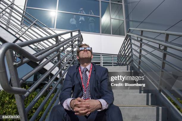 Man in a suit wears solar viewing glasses while looking at the sun during a solar eclipse at the California Independent System Operator headquarters...