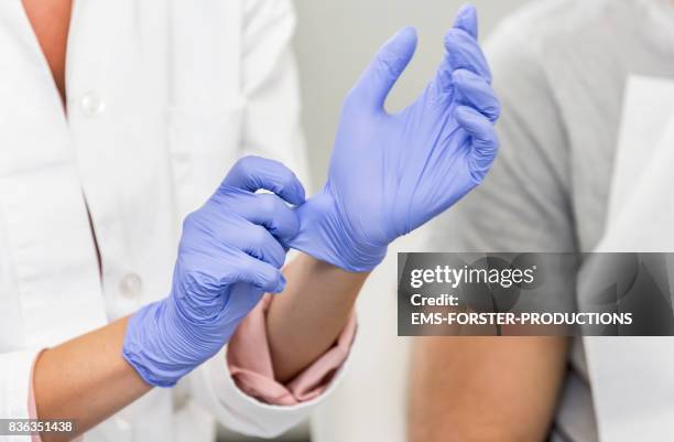 female dentist is putting on some blue, latex, one use examination gloves while she is talking with her patient - rubber gloves stockfoto's en -beelden