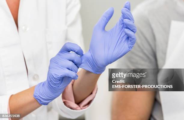 female dentist is putting on some blue, latex, one use examination gloves while she is talking with her patient - surgical glove stock pictures, royalty-free photos & images