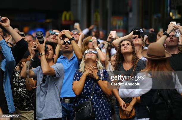 People gather to observe the total solar eclipse with solar eclipse glasses and cameras at the Times Square in New York City, United States on August...