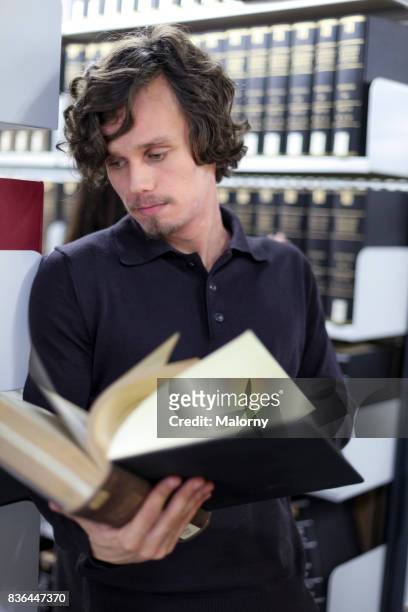 young man reading a book in the library. student, university. - association of religion data archives stock pictures, royalty-free photos & images