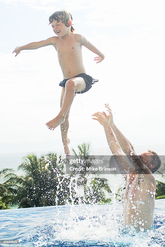Father playfully tossing son in air in pool