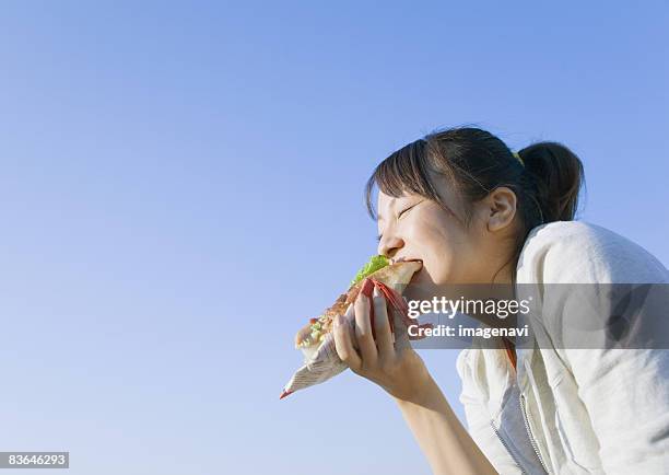 a woman eating a hotdog - asian eating hotdog stockfoto's en -beelden