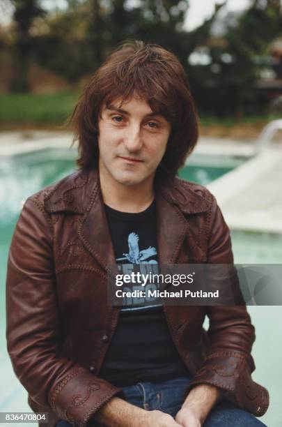 English singer-songwriter and former Wings and Moody Blues guitarist, Denny Laine posed wearing a leather jacket outside in a garden in front of a...