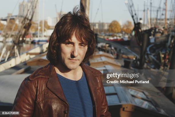 English singer-songwriter and former Wings and Moody Blues guitarist, Denny Laine posed wearing a leather jacket outside near an harbor 1981.