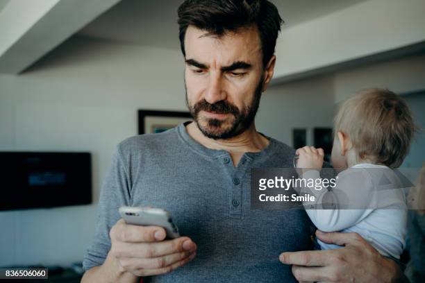 Father holding baby reading phone