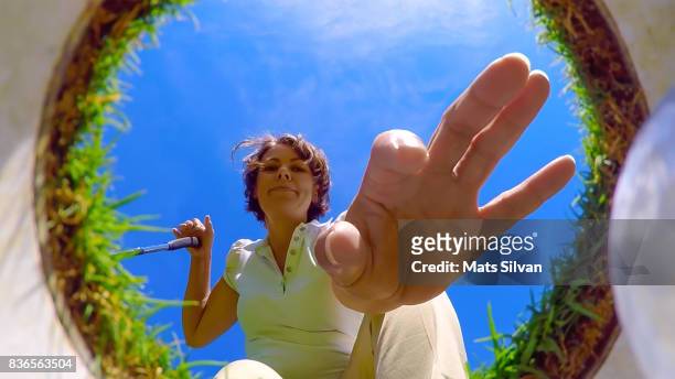 woman picking up her golf ball from the hole - naderen stockfoto's en -beelden