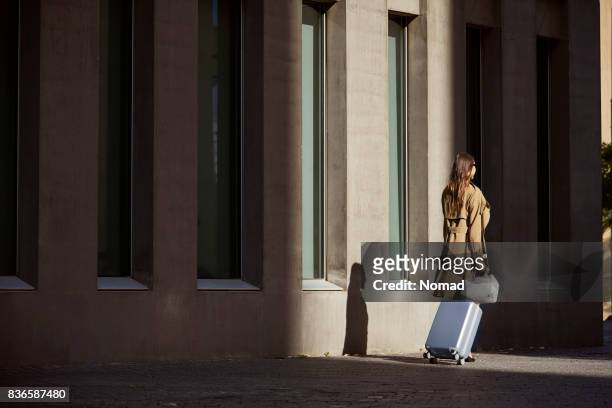 rear view of executive with bags outside airport - trench coat back stock pictures, royalty-free photos & images