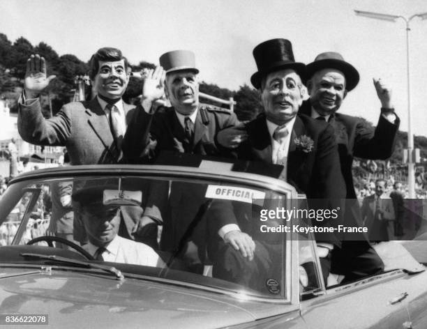 Quatre personnes dans une voiture décapotable portant les masques de McMillan, Kennedy, Khrouchtchev et de Gaulle saluent la foule, à Jersey en août...