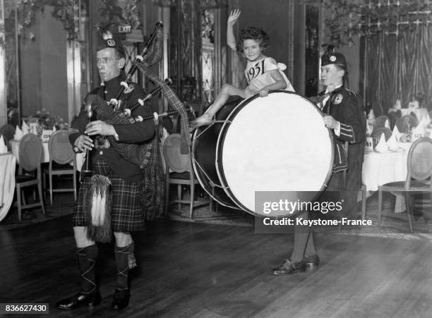 Une petite fille s'amuse, perchée sur la grosse caisse d'un musicien écossais, derrière un joueur de cornemuse, lors des préparatifs dans une salle...