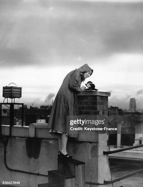 Desiree Jestico, employée du ministère de l'Air anglais, en imperméable et capuche, collecte des données sur le toit du ministère enregistrées par...