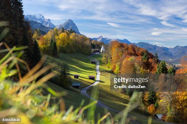 scenic view over road leading to wamberg village with zugspitze and wetterstein mountain range in the background, werdenfelser land, upper bavaria, germany - バーバリアンアルプス ストックフォトと画像