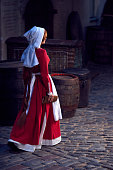 Townswoman in red dress with an apron and chaperone on the street. Costume stylized of later Middle Ages on 15/ 16th century.