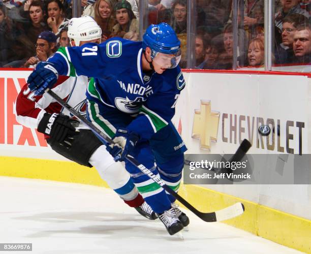 Mason Raymond of the Vancouver Canucks watches a bouncing puck along the boards with Adam Foote of the Colorado Avalanche on his tail during their...
