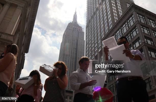 People use various methoods to view the sun being eclipsed by the moon over top of the Empire State Building in New York City on August 21, 2017.