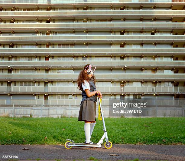 girl wearing zebra mask riding scooter on housing estate   - newnaivetytrend stock-fotos und bilder