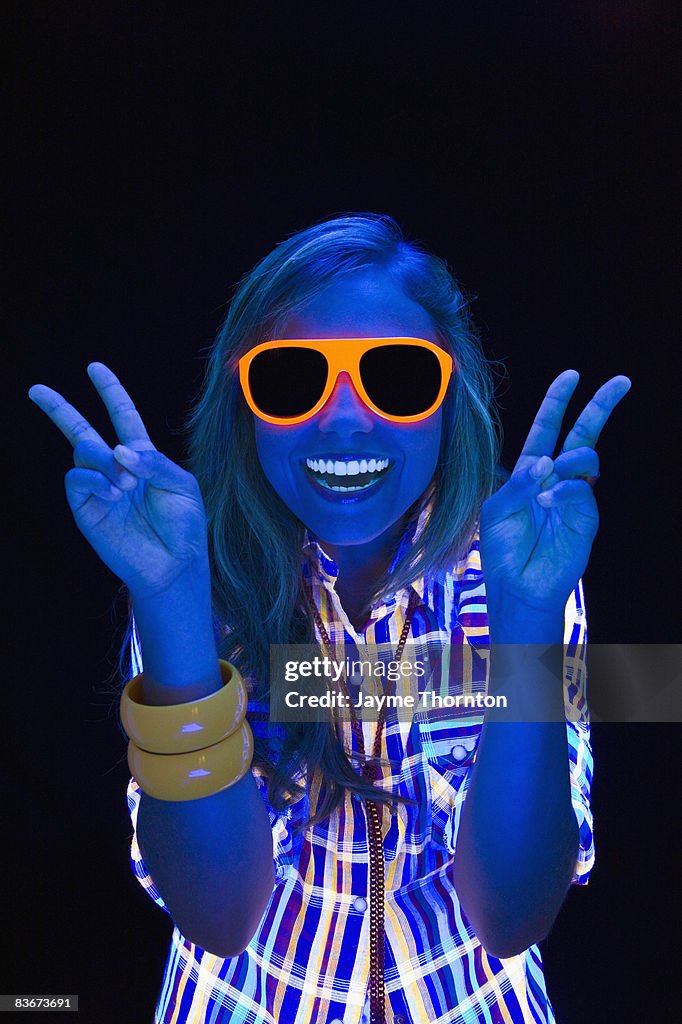 Woman giving peace sign under blacklights