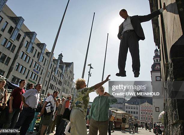 In a file picture dated April 27 pedestrians look at German artist Johan Lorbeer showing his still-life performance "Tarzan-Standbein" on the facade...