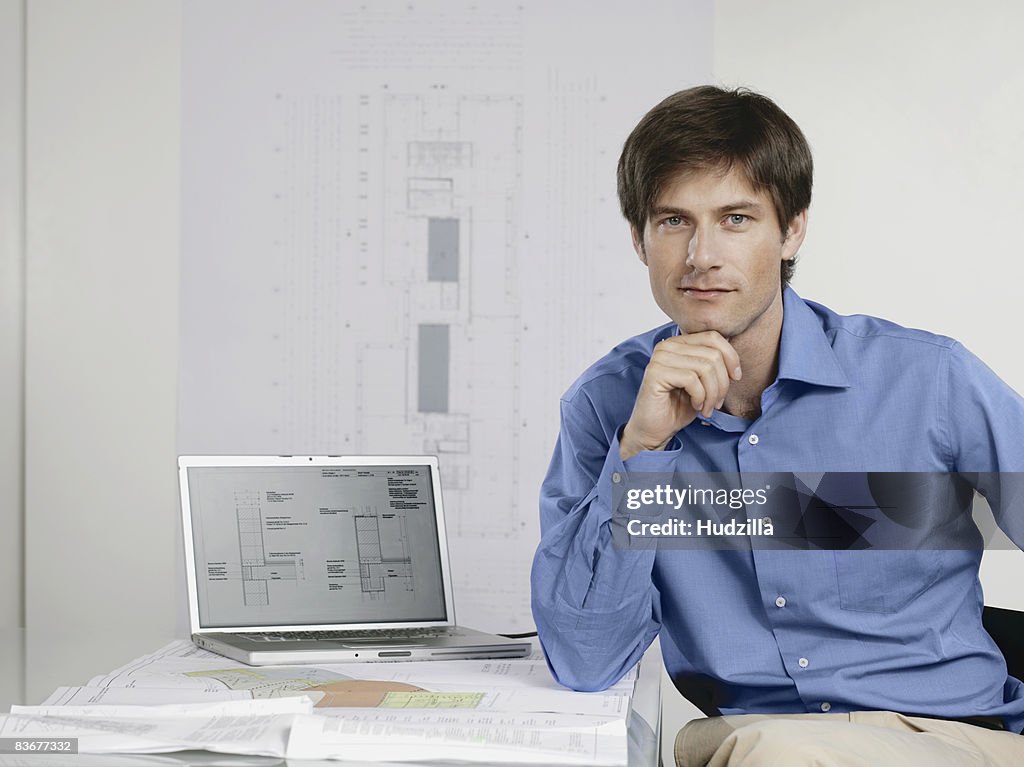An architect sitting at his desk with a laptop and architectural drawings