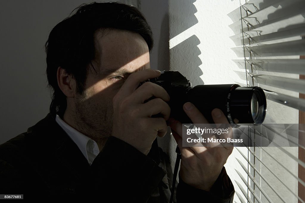 A man looking through blinds with a camera