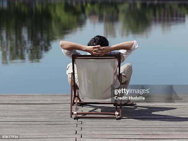 rear view of a man sitting in a deck chair on a jetty - hands behind head stock pictures, royalty-free photos & images