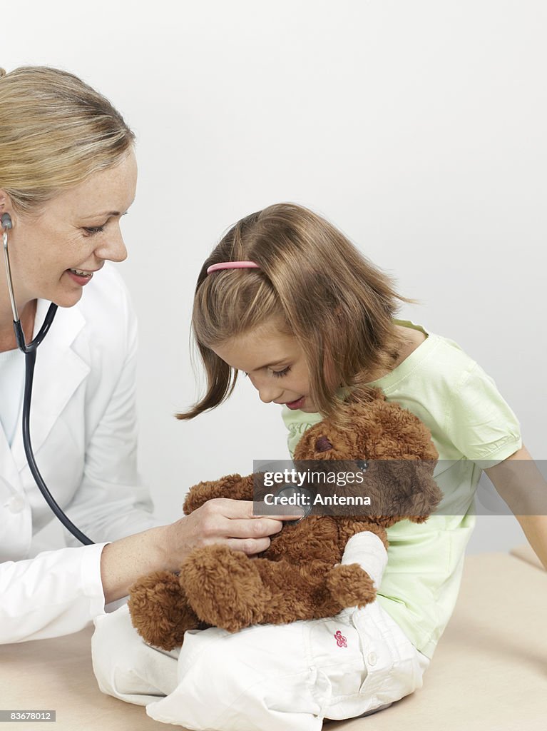 Female pediatrician examining a girl's teddy bear
