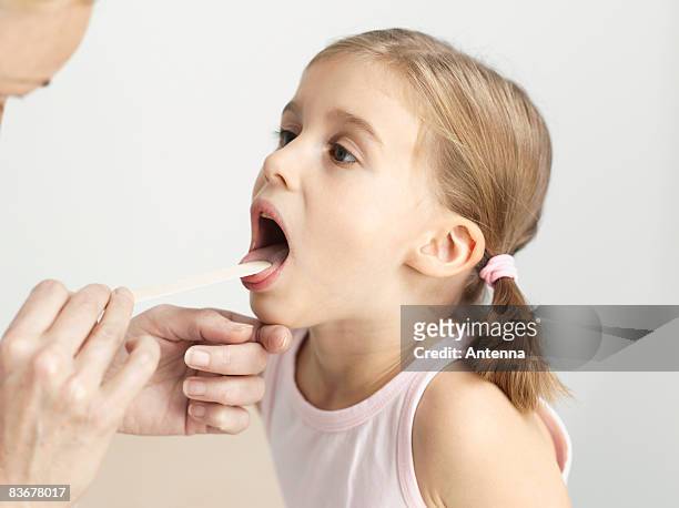 a young girl having her throat examined with a tongue depressor - girl tongue doctor stockfoto's en -beelden