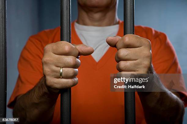 a prisoner standing behind prison bars - prison clothes stock pictures, royalty-free photos & images
