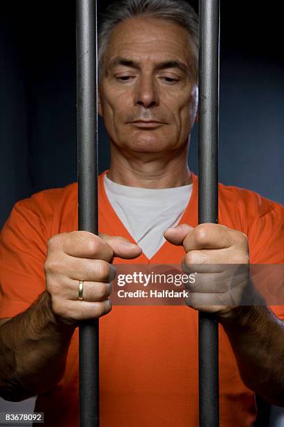 a prisoner standing behind prison bars - prison clothes stock pictures, royalty-free photos & images