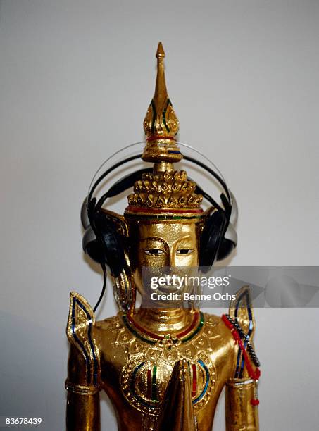 a praying gold buddha statue with headphones on - buddha stock-fotos und bilder