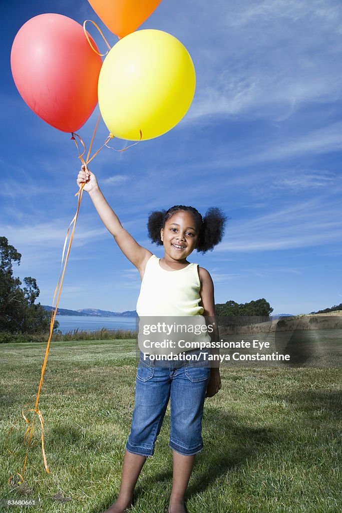 Little girl standing, holding on to balloons