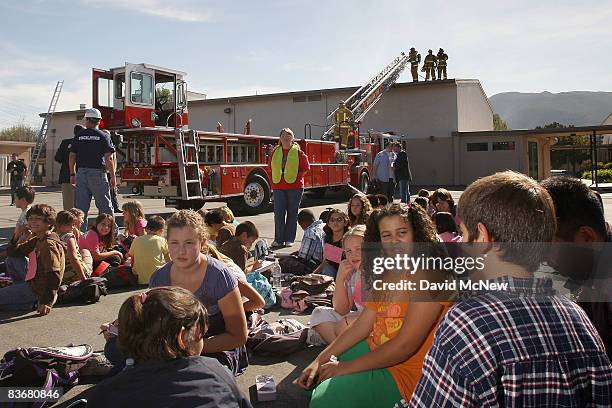 Firefighters drill atop a simulated burning school auditorium as students of Stevenson Elementary School gather on the playground during the...