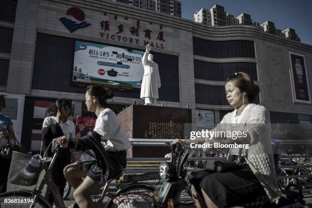 Commuters on bicycles ride past a statue of Mao Zedong displayed in front of the Baotou Victory Shopping Mall in Baotou, Inner Mongolia, China, on...