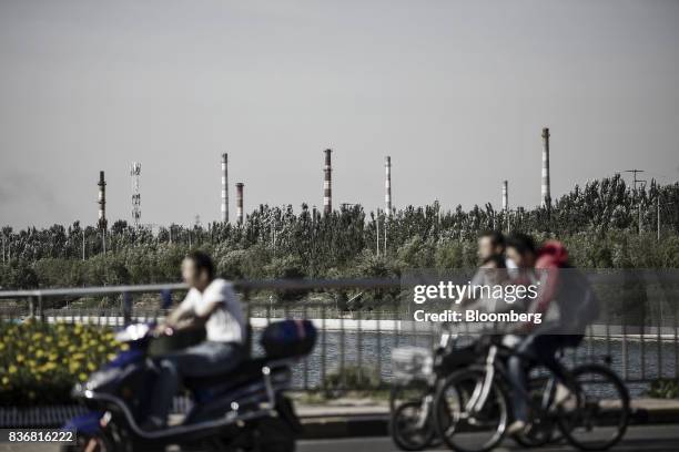 People ride on bicycles past the smoke stacks of factories and power plants in Baotou, Inner Mongolia, China, on Friday, Aug. 11, 2017. China's...