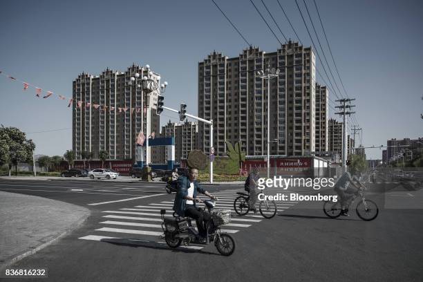 Commuters ride on bicycles past residential buildings in Baotou, Inner Mongolia, China, on Friday, Aug. 11, 2017. China's economy showed further...