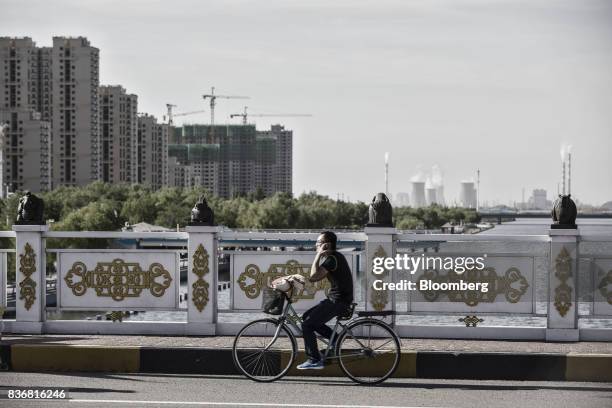 Man rides a bicycle over a bridge as residential buildings and power plants stand in the distance in Baotou, Inner Mongolia, China, on Friday, Aug....